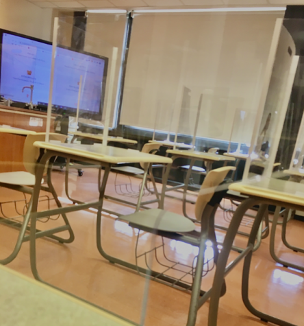 Desks in a Post science classroom encased in plexiglass shields.