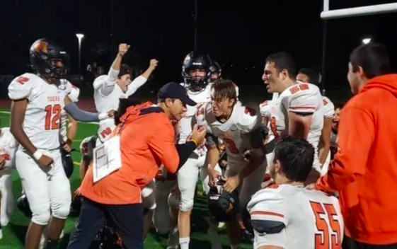 Coach Vitti encourages the Varsity Football team in a huddle before they head back to the field.